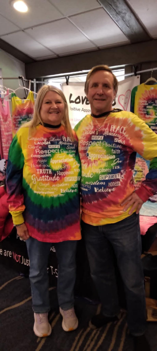 Two people wearing Love Lingo 7-Chakra color long-sleeve rainbow tie-dye tees, designed as energy-based apparel to align vibrational frequency.